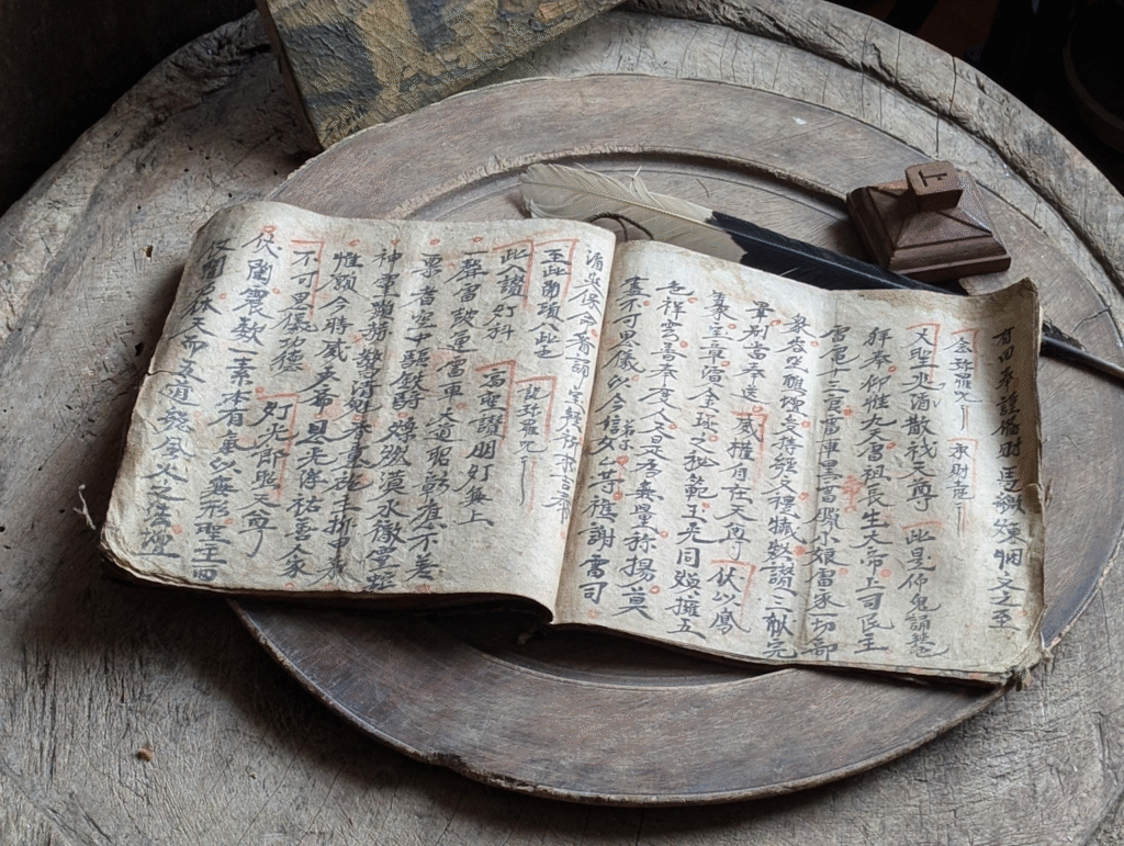 Traditional East Asian manuscript with calligraphy alongside a quill pen on wooden surface, symbolizing the craft of historical writing and attention to authentic cultural details