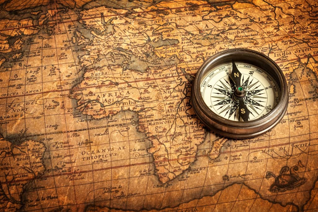 Vintage brass compass positioned on weathered antique world map with navigation routes, symbolizing the journey authors take to guide readers through unexplored historical territories and untold stories