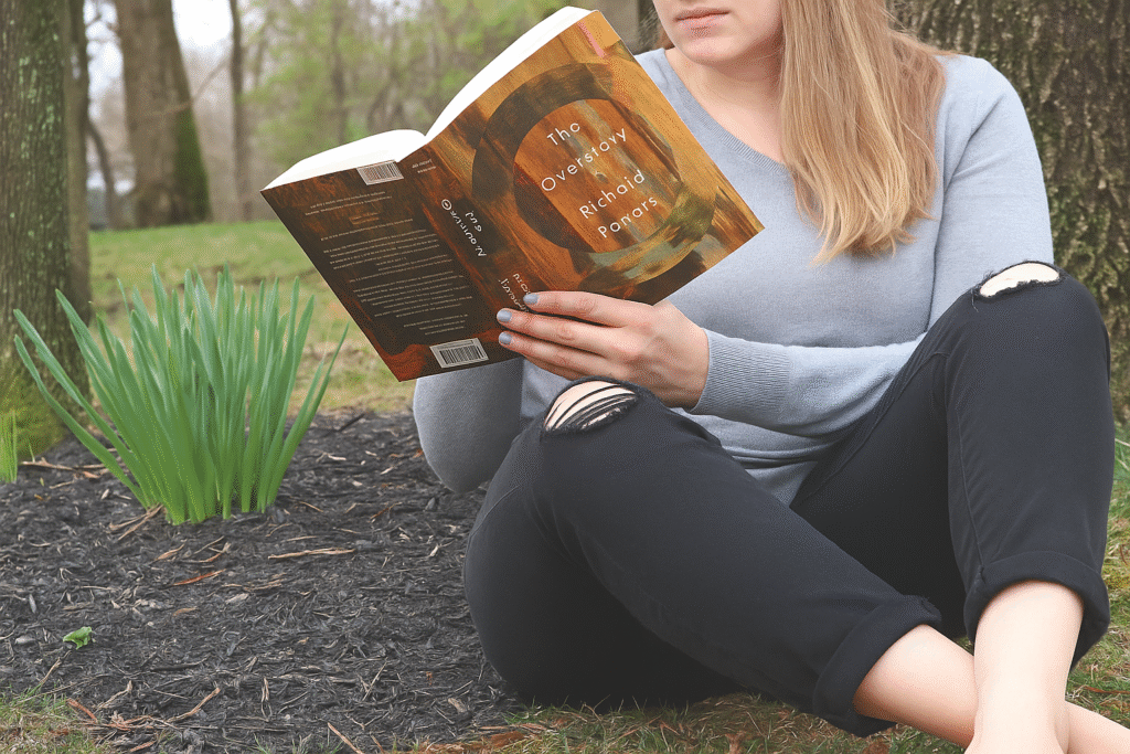 A person reading The Overstory by Richard Powers outdoors, highlighting the book's climate fiction genre 