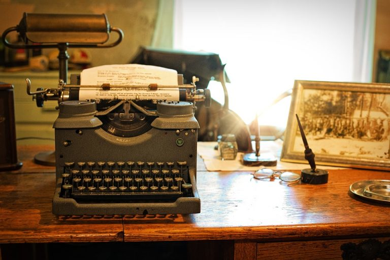 A vintage writer's desk featuring a classic typewriter, manuscript, and traditional writing tools in a warm, nostalgic setting