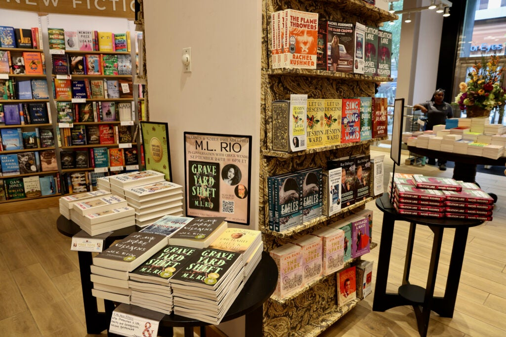Interior of bookstore showing organized book displays on round tables and shelving units with featured author events and new fiction sections