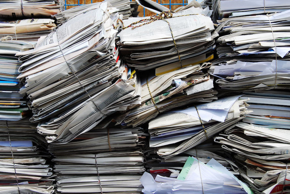 Multiple stacks of bundled newspapers and papers tied with strings, organized in piles for recycling collection rather than landfill disposal