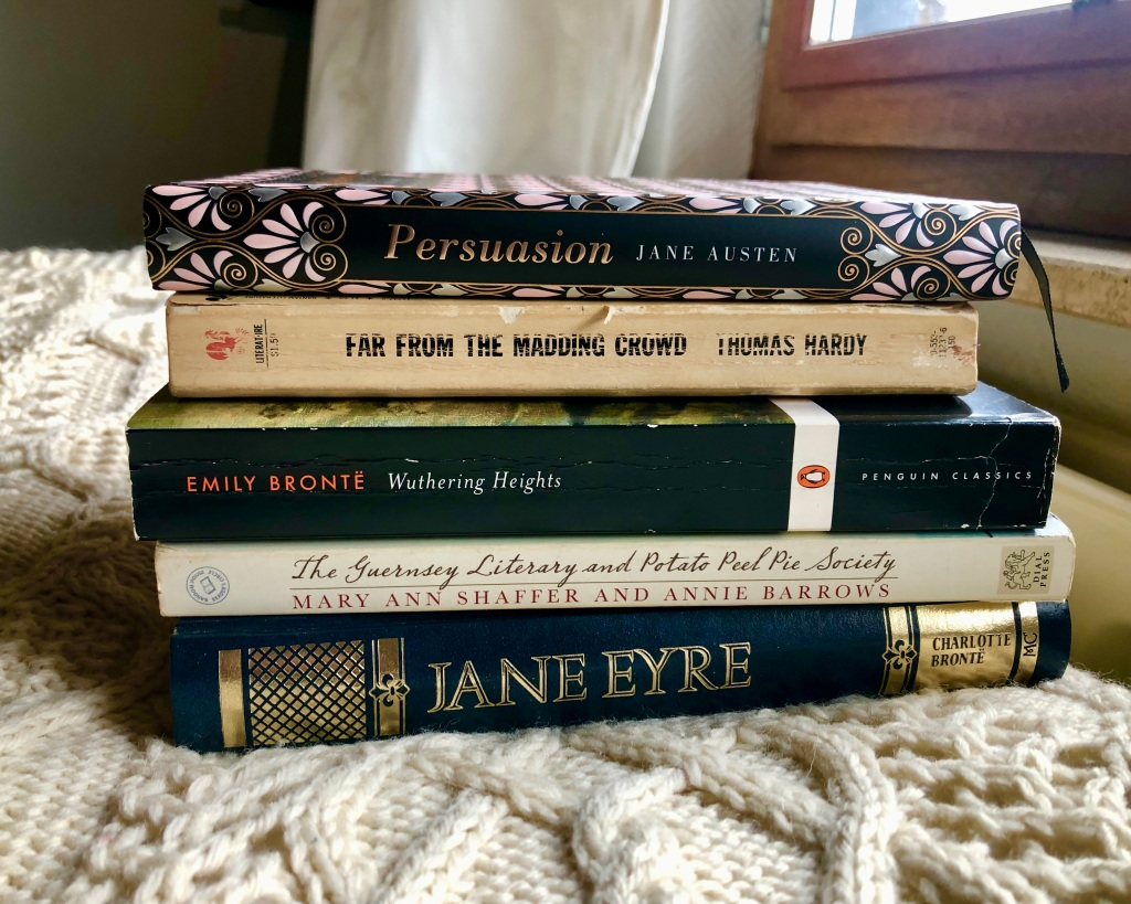 Stack of classic novels including Persuasion, Wuthering Heights, and Jane Eyre positioned by window on knitted blanket, suggesting classic literature revival
