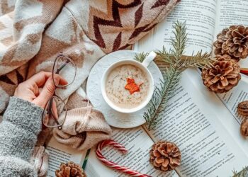 Cozy winter reading scene featuring an open book with pine cones, hot cocoa mug, soft blanket