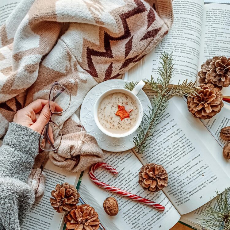 Cozy winter reading scene featuring an open book with pine cones, hot cocoa mug, soft blanket