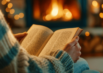 Close-up of reader in knitted sweater holding book by fireplace showing intimate comfort reading experience