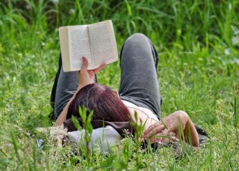 Woman reading book on grass in summer relaxation resembling emotional pacing in storytelling