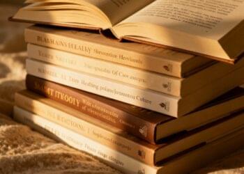 The image shows a carefully arranged stack of personal development books bathed in warm, golden light, perfectly capturing the essence of bibliotherapy as healing and transformative