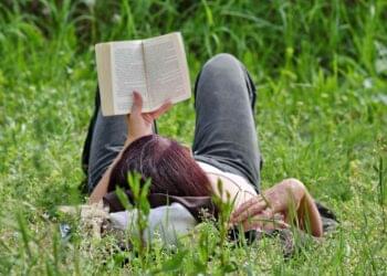 Woman reading book on grass in summer relaxation resembling emotional pacing in storytelling